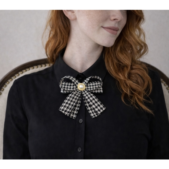 Elegancka broszka w formie kokardy w klasyczny wzór pepitki, wykończona perłowym środkiem – ponadczasowy dodatek do stylowych stylizacji.