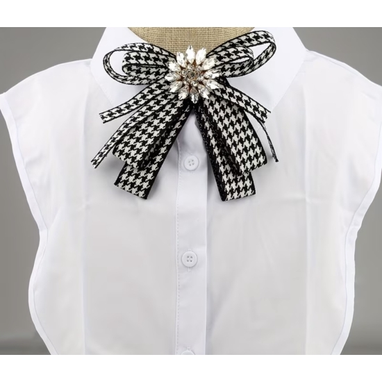 Stylowa broszka w formie kokardy w klasyczny wzór pepitki, ozdobiona efektownym kryształowym środkiem – elegancki detal, który przyciąga spojrzenia.