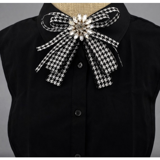 Stylowa broszka w formie kokardy w klasyczny wzór pepitki, ozdobiona efektownym kryształowym środkiem – elegancki detal, który przyciąga spojrzenia.