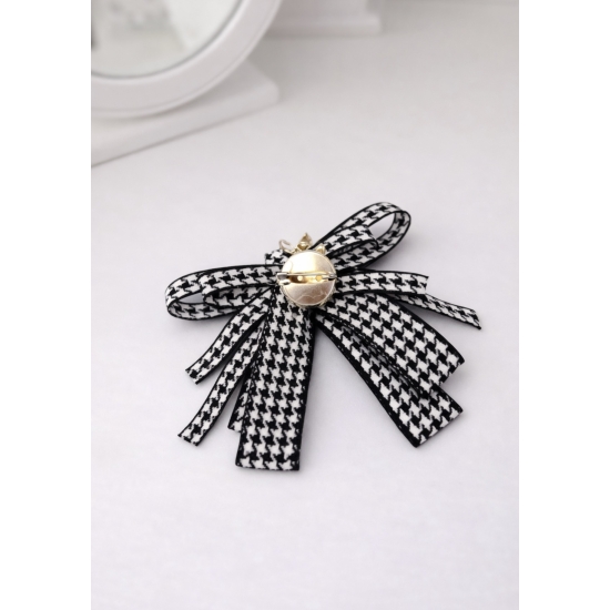 Stylowa broszka w formie kokardy w klasyczny wzór pepitki, ozdobiona efektownym kryształowym środkiem – elegancki detal, który przyciąga spojrzenia.