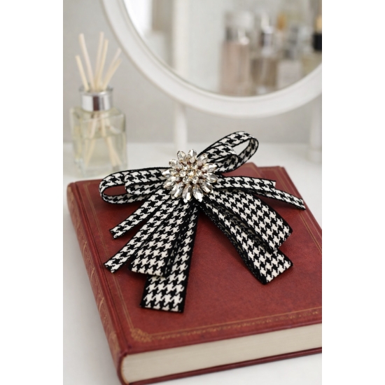 Stylowa broszka w formie kokardy w klasyczny wzór pepitki, ozdobiona efektownym kryształowym środkiem – elegancki detal, który przyciąga spojrzenia.