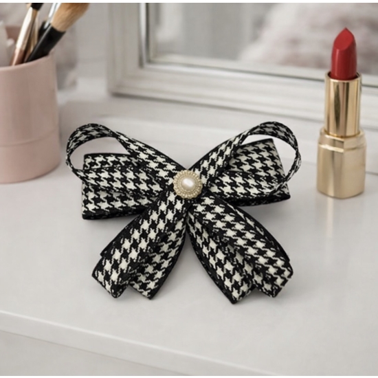 Elegancka broszka w formie kokardy w klasyczny wzór pepitki, wykończona perłowym środkiem – ponadczasowy dodatek do stylowych stylizacji.