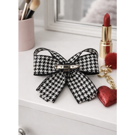 Elegancka broszka w formie kokardy w klasyczny wzór pepitki, wykończona perłowym środkiem – ponadczasowy dodatek do stylowych stylizacji.