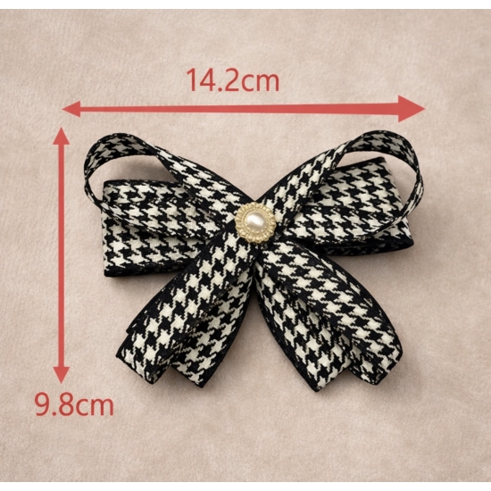 Elegancka broszka w formie kokardy w klasyczny wzór pepitki, wykończona perłowym środkiem – ponadczasowy dodatek do stylowych stylizacji.